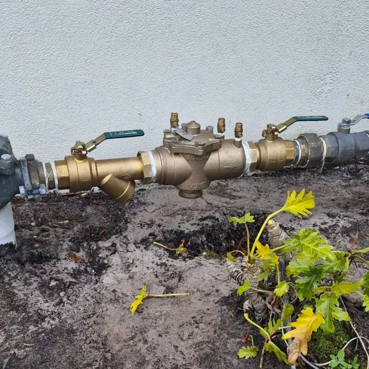 A brass testable backflow device on a water line at a garden edge