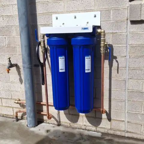 Twin blue water filter housings on a painted block wall
