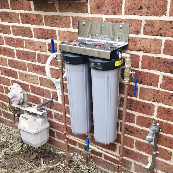 Twin cartridge filter housings on brick beside the gas meter