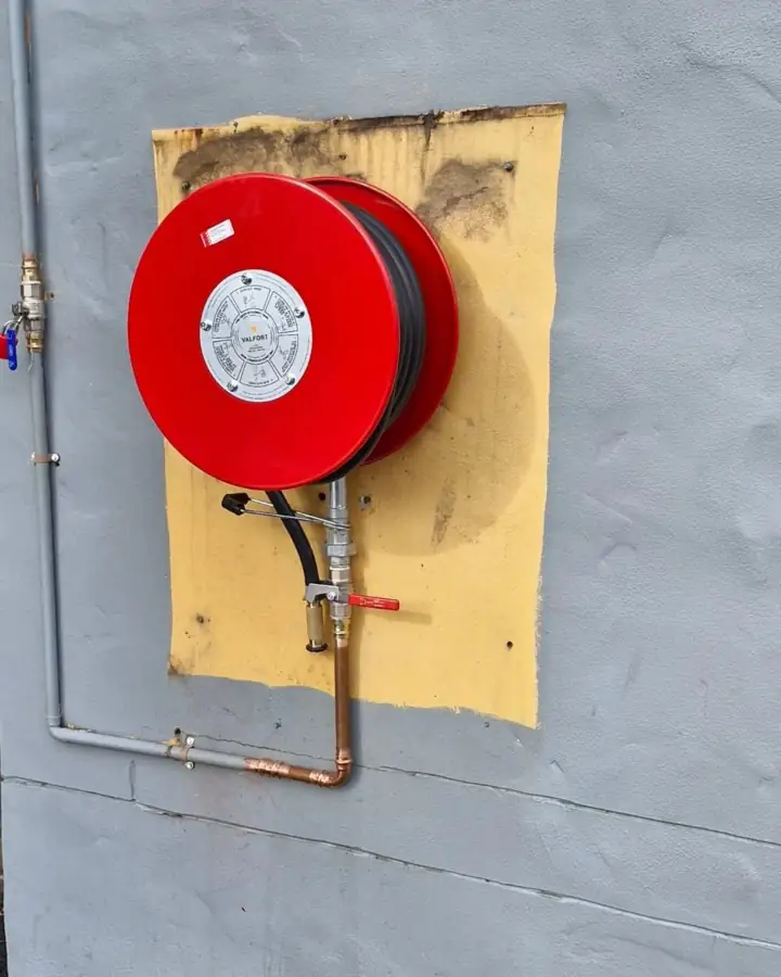 A red fire hose reel mounted on a grey rendered wall