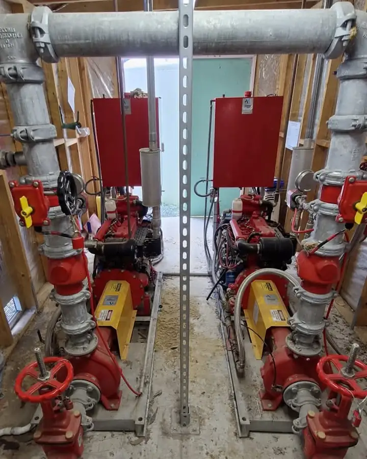 Two fire pump sets side by side in a pump room, red pumps and engines under galvanised pipework, with red valve handwheels in front