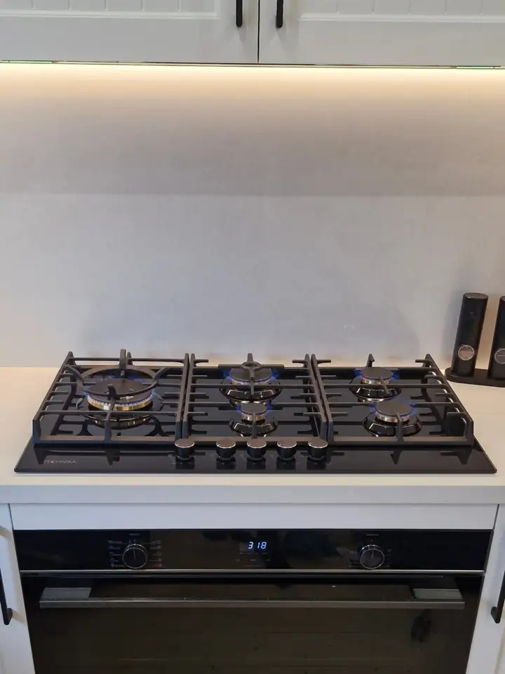 A gas cooktop over a wall oven in a new kitchen