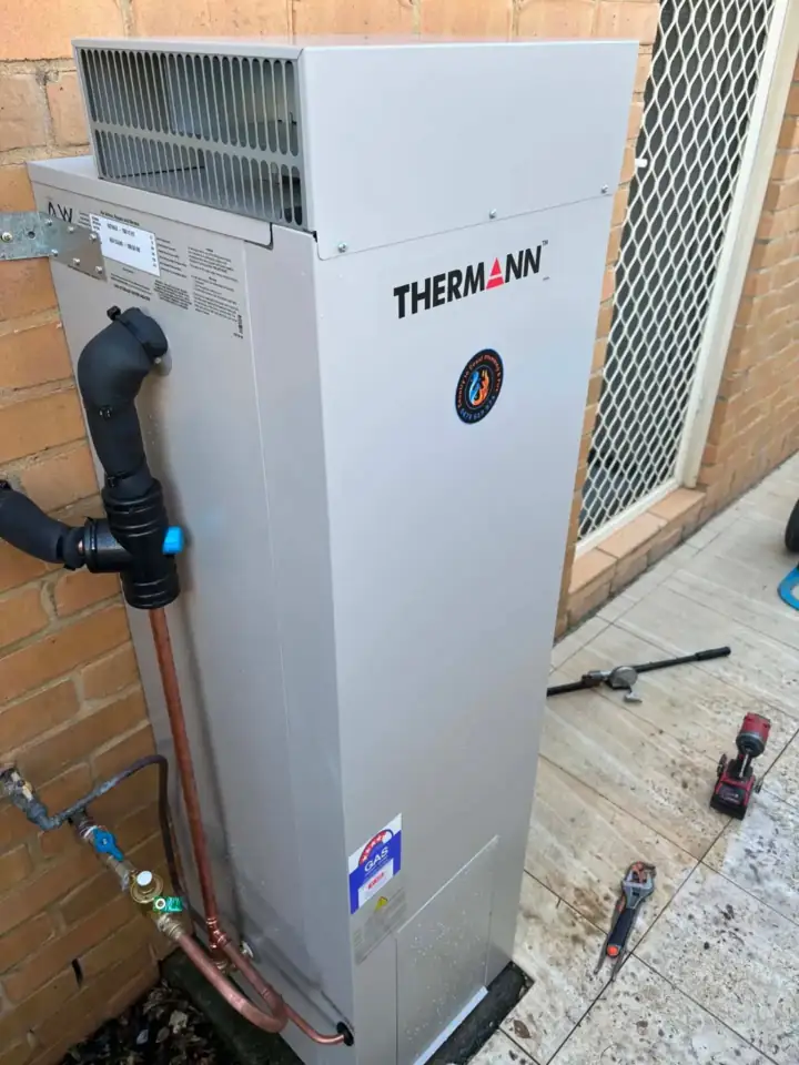 A tall heat pump hot water unit against a brick wall