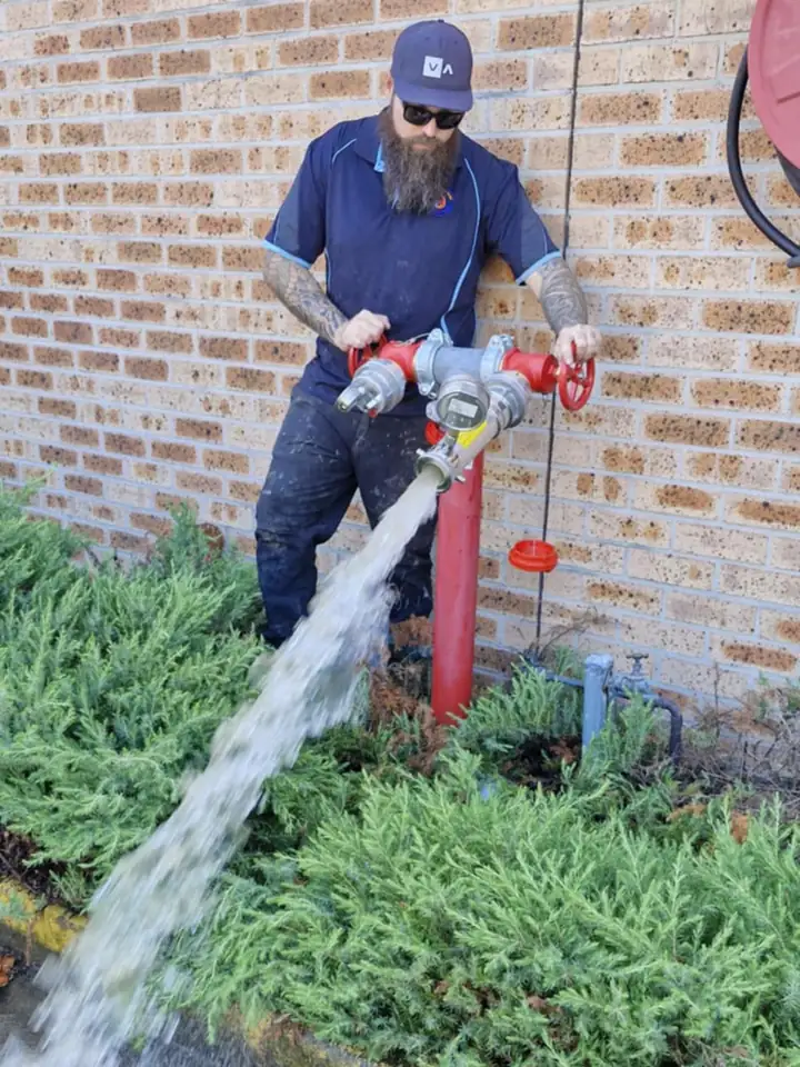 A tradesman opening a twin-outlet hydrant, water flowing across the garden bed