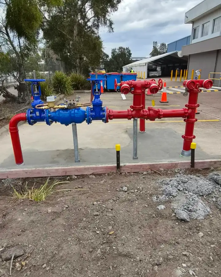 A hydrant booster set-up on a commercial site: blue valves and red pipework with hydrant outlets on a fresh concrete pad