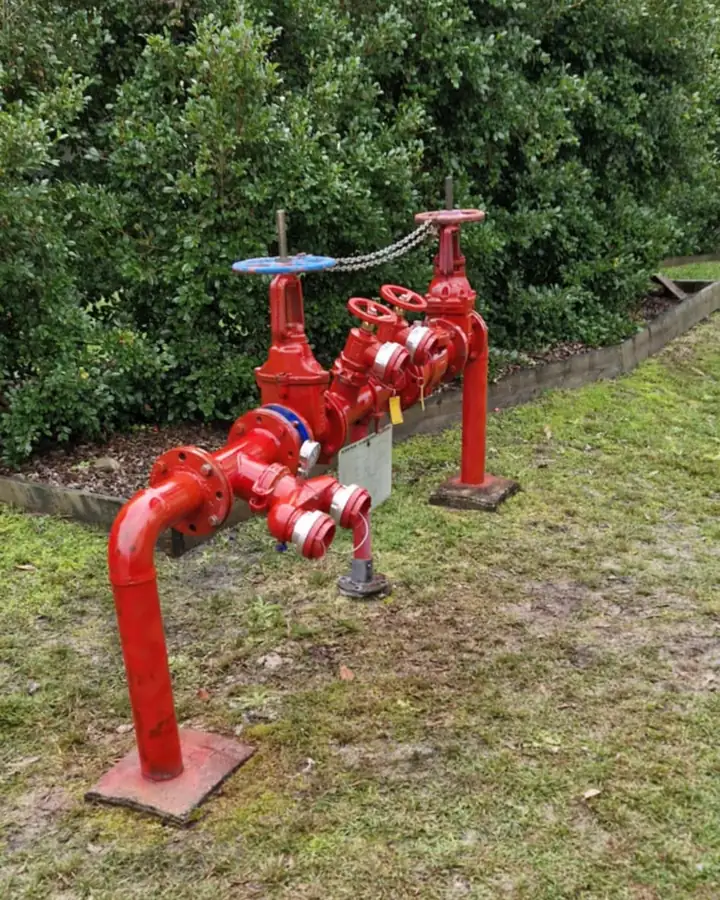 A red valve set on a lawn beside a hedge
