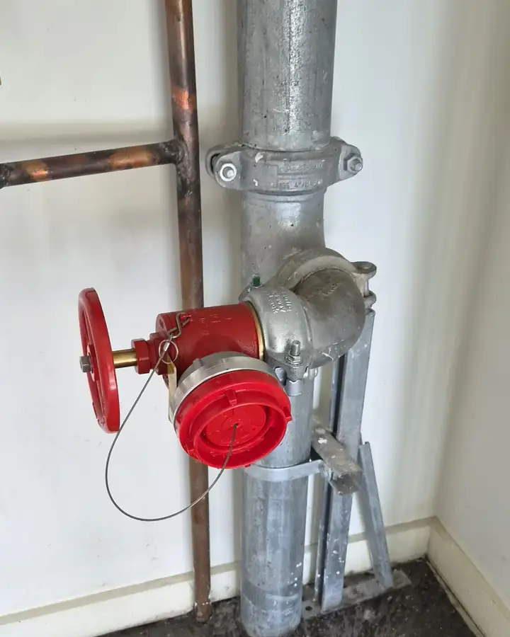 A hydrant landing valve on a galvanised riser inside a building