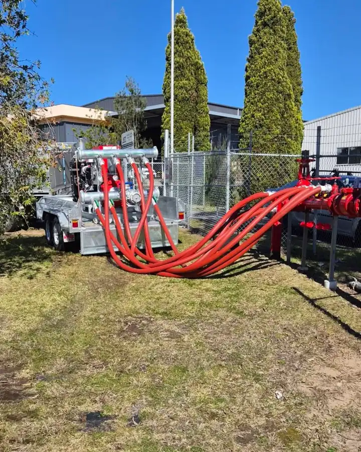 Our test trailer with red hoses laid across the grass to a booster behind a fence