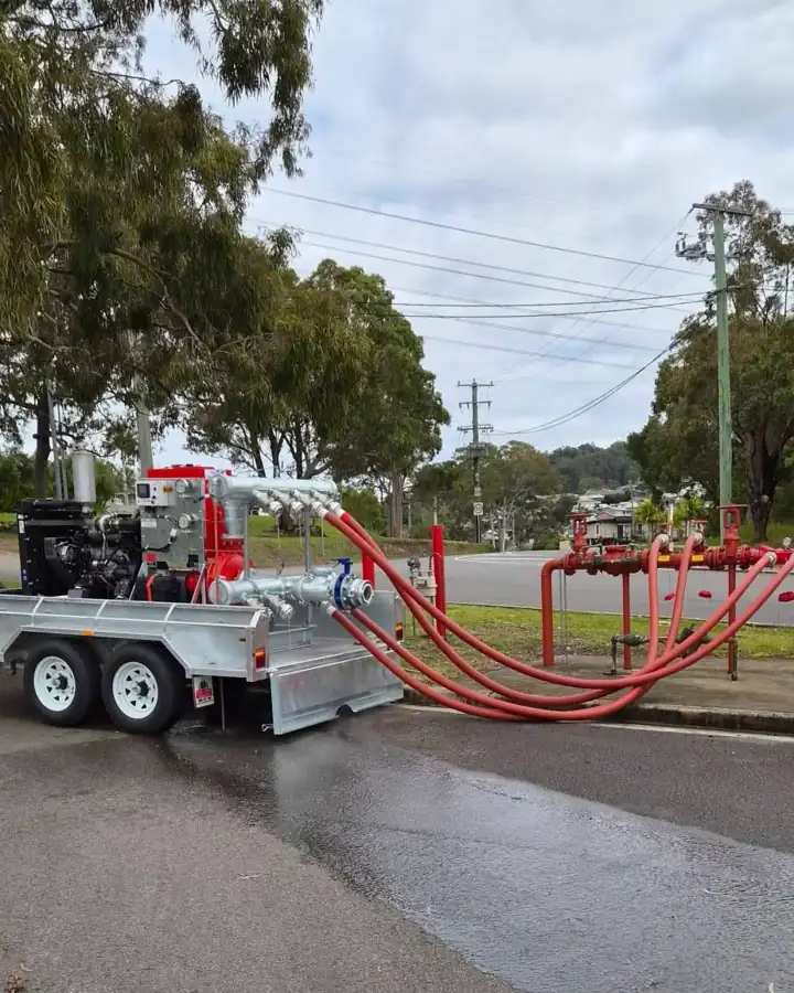 Our pump trailer parked on a wet road, red hoses running from its manifold to a kerbside booster