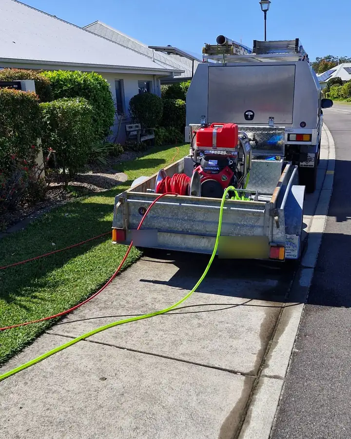 Our sewer jetter on its trailer at the kerb, a petrol engine and a red hose reel on board, with red and green hoses run across the footpath to the house