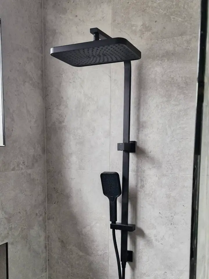 A black shower rail with a rain head on grey tiles