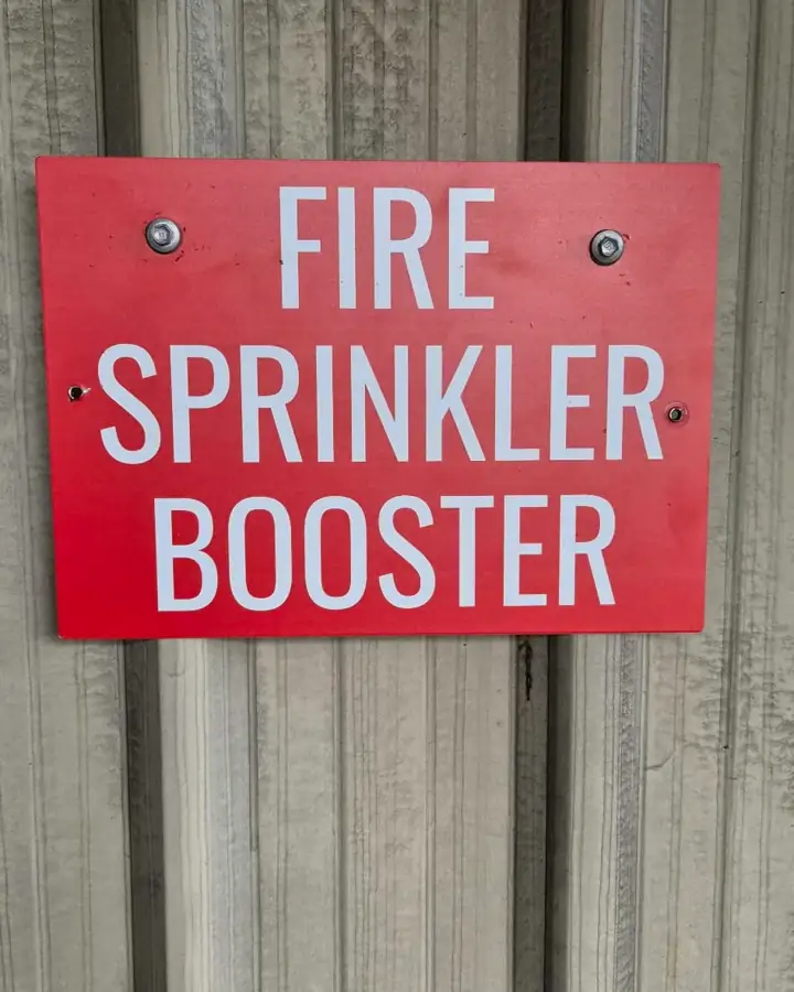 A red FIRE SPRINKLER BOOSTER sign on wall cladding